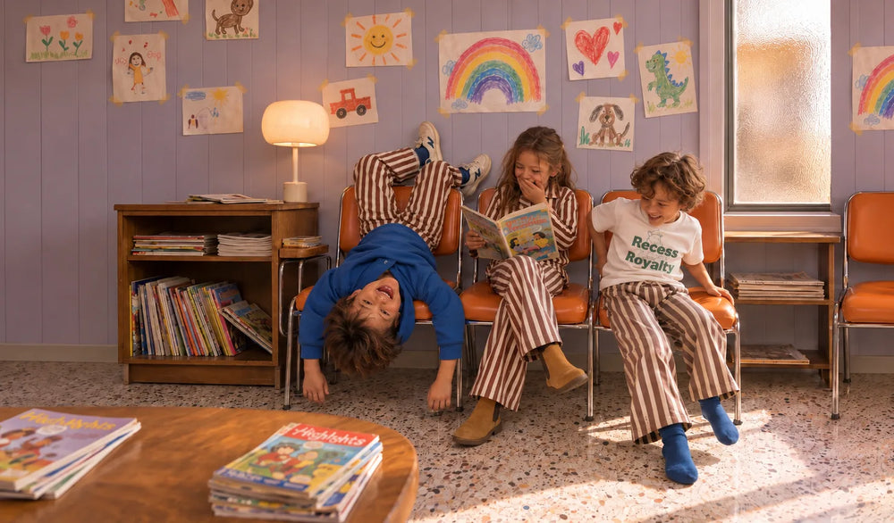 Three siblings in matching brown and cream striped Trouzers goofing around in a waiting room with rainbow drawings on the wall