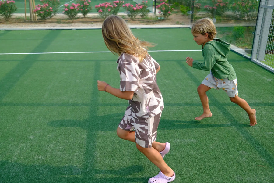 Two kids running across the grass court